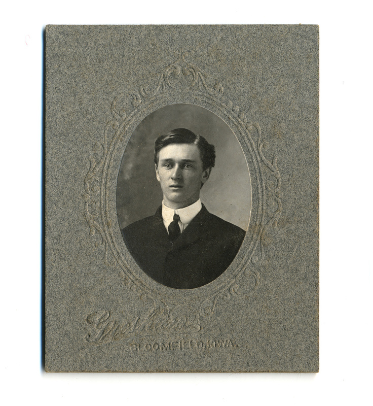 Retrato de busto de un hombre joven, de tez clara y mirada serena hacia un costado. Viste una chaqueta de traje oscura, camisa blanca de cuello alto rígido y una corbata oscura de nudo sencillo. La imagen está capturada en un estudio fotográfico profesional, enmarcada en un óvalo con bordes ornamentales grabados en relieve sobre un soporte de cartón gris texturizado.