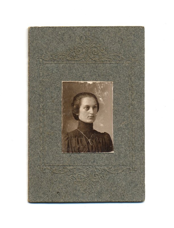 Retrato de estudio de una mujer joven captada en un plano medio corto. La figura presenta un peinado recogido y viste una prenda oscura de cuello alto con detalles de pliegues verticales en el pecho, estilo característico de la moda femenina de finales del Porfiriato. La imagen central está montada sobre un cartón decorado con motivos ornamentales.