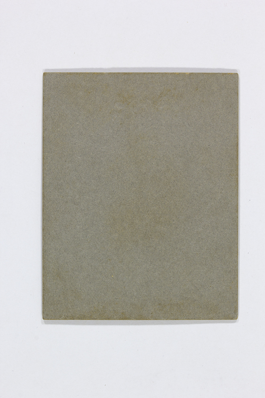 Vista posterior de una pieza fotográfica antigua. La imagen muestra únicamente el reverso de un soporte rígido, sin inscripciones, sellos de fotógrafo ni marcas manuscritas. Se aprecia la textura granulada y el desgaste natural en los bordes de un material de gramaje alto, probablemente cartón prensado de uso comercial.