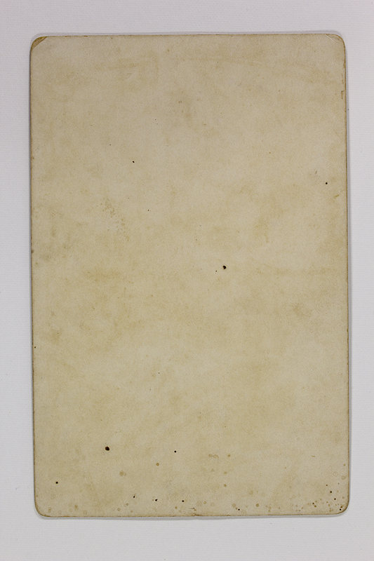 Esta imagen documenta el reverso de un soporte fotográfico histórico, posiblemente una tarjeta de gabinete o postal antigua. No contiene información visual, manuscrita ni sellos de fotógrafo, mostrando únicamente el desgaste natural del papel, el cual presenta una pátina amarillenta y manchas de oxidación ácida (foxing) consistentes con materiales de finales del siglo XIX.