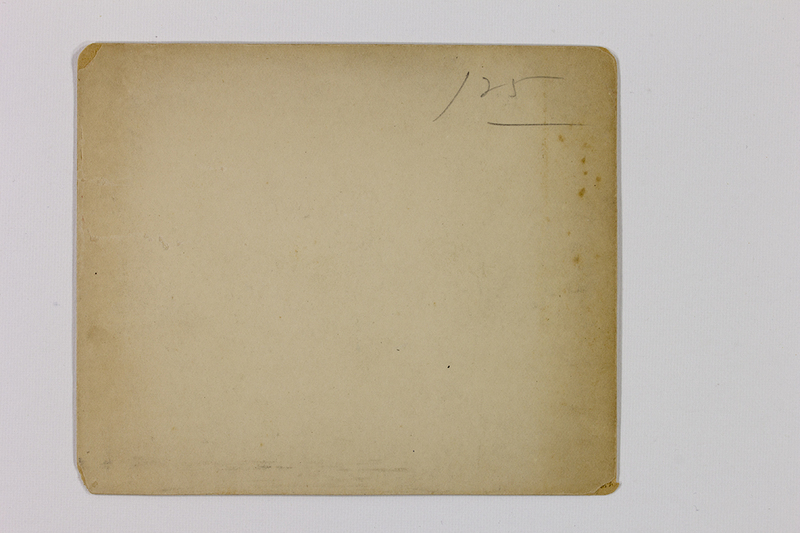 Vista posterior de una fotografía histórica sobre soporte de papel. Presenta un tono amarillento debido a la oxidación de la celulosa y el paso del tiempo, con presencia de manchas de oxidación o humedad tipo foxing. Se observa una marca manuscrita a lápiz en el cuadrante superior derecho con la cifra '125', indicativa de una clasificación de inventario o control archivístico.