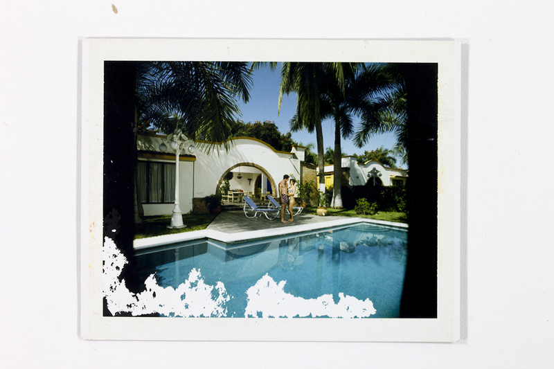 Escena de recreación en una villa o resort con arquitectura de estilo neocolonial. Una pareja joven en trajes de baño se encuentra junto a una piscina de aguas cristalinas que refleja la construcción. El entorno está decorado con palmeras y una luminaria ornamental, evocando el estilo de vida vacacional de la clase media-alta en el México de los años setenta.