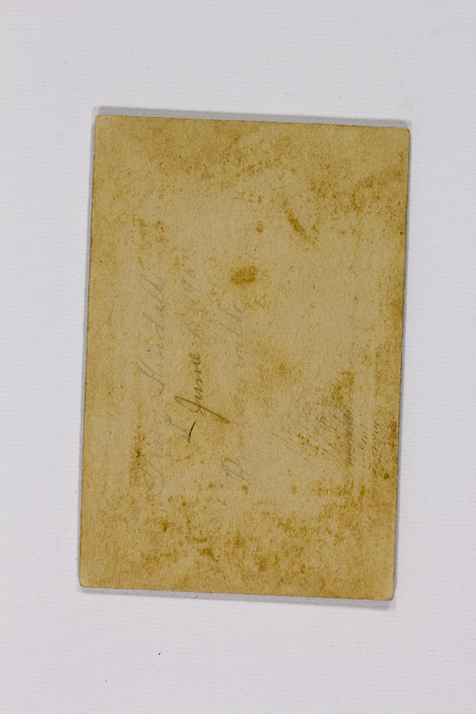 Reverso de una fotografía histórica montada sobre cartón rígido. Presenta inscripciones manuscritas a lápiz que incluyen un nombre propio y la fecha 'June 1907'. El soporte muestra signos de envejecimiento natural, como amarillamiento por oxidación de la lignina y manchas de foxing, lo que constituye un registro de su procedencia y temporalidad.