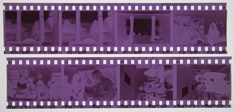 Dos tiras de película negativa de 35mm con escenas de interiores que documentan la vida cotidiana contemporánea. Se observa a una persona trabajando frente a una computadora portátil, así como diversas tomas de un establecimiento público, posiblemente una cafetería o restaurante, donde personas interactúan en un entorno social urbano de finales del siglo XX o inicios del XXI.