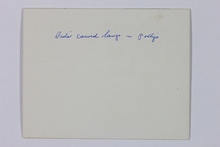 Se trata del reverso de una fotografía histórica con una anotación manuscrita en tinta azul que reza 'Dads' carved lamp ~ Pollys'. El texto indica que la imagen en el anverso documenta un objeto decorativo o artesanal dentro de un contexto doméstico y familiar, probablemente para fines de inventario o recuerdo personal.