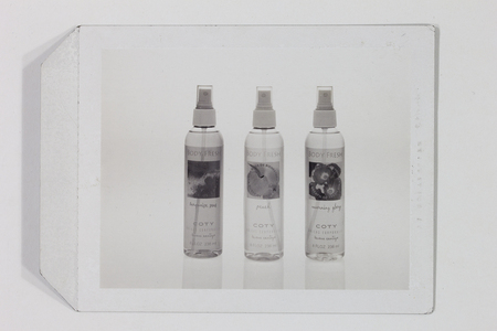 Fotografía publicitaria de estudio que muestra tres envases de atomizador 'Body Fresh' de la marca Coty, alineados verticalmente. Las fragancias identificadas son Turquoise Seas, Peach y Morning Glory. Cada botella presenta etiquetas con texto bilingüe en inglés y español, destacando el eslogan 'llévame contigo'. Se trata de una toma de producto en blanco y negro con iluminación controlada.