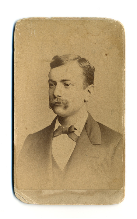Retrato de estudio de un hombre joven con bigote poblado, captado en plano medio corto y vista de tres cuartos. Viste indumentaria formal masculina de finales del siglo XIX, consistente en un saco oscuro, chaleco a juego, camisa de cuello r!gido y un corbat!n de lazo oscuro. La imagen refleja la sobriedad t!pica del retrato social decimon3nico.