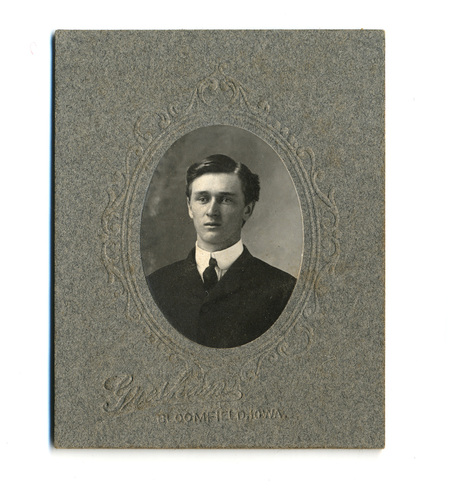 Retrato de busto de un hombre joven, de tez clara y mirada serena hacia un costado. Viste una chaqueta de traje oscura, camisa blanca de cuello alto rígido y una corbata oscura de nudo sencillo. La imagen está capturada en un estudio fotográfico profesional, enmarcada en un óvalo con bordes ornamentales grabados en relieve sobre un soporte de cartón gris texturizado.