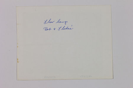 Reverso de una fotografía instantánea con una anotación manuscrita en tinta azul que reza 'floor lamp, Bob & Leda's'. El documento presenta el sello de fábrica 'POLAROID' y un código de producción 'J602E2A' en el borde inferior, además de pequeñas manchas de oxidación o residuos de adhesivo en el margen izquierdo.