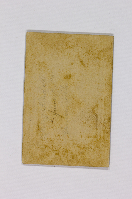 Reverso de una fotografía histórica montada sobre cartón rígido. Presenta inscripciones manuscritas a lápiz que incluyen un nombre propio y la fecha 'June 1907'. El soporte muestra signos de envejecimiento natural, como amarillamiento por oxidación de la lignina y manchas de foxing, lo que constituye un registro de su procedencia y temporalidad.