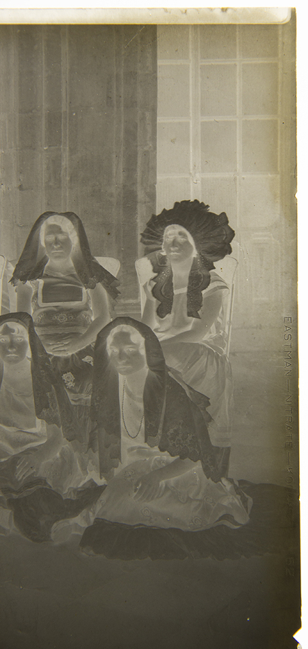 La imagen muestra a un grupo de cuatro mujeres ataviadas con indumentaria tradicional, posiblemente del Istmo de Tehuantepec, destacando el uso de mantillas de encaje y un tocado de resplandor. Posan sentadas en un espacio interior de techos altos con una columna de piedra y un ventanal al fondo, sugiriendo un retrato formal en un recinto histórico o gubernamental.