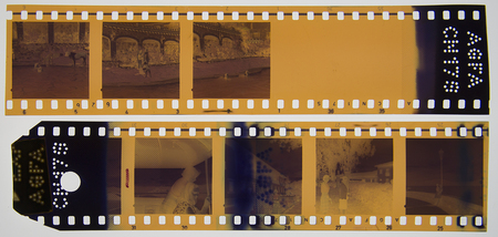 Dos tiras de negativos de 35mm que documentan una reunión o visita en un entorno profesional de carácter científico o académico. Aparecen hombres y mujeres adultos con vestimenta formal y batas de laboratorio, portando identificaciones y consultando documentos. Se incluyen vistas de interiores con estanterías de libros y tomas de exteriores a través de ventanales.