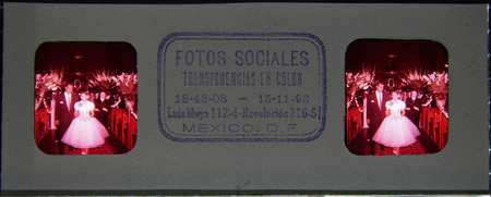 Una escena doméstica captura una celebración infantil, posiblemente un cumpleaños, en el México de mediados del siglo XX. Un grupo de niños y jóvenes rodea una mesa dispuesta con un gran pastel de varios niveles y vasos con bebidas. La vestimenta, que incluye camisas abotonadas y diademas, refleja las convenciones sociales y la moda de la clase media urbana de la época.